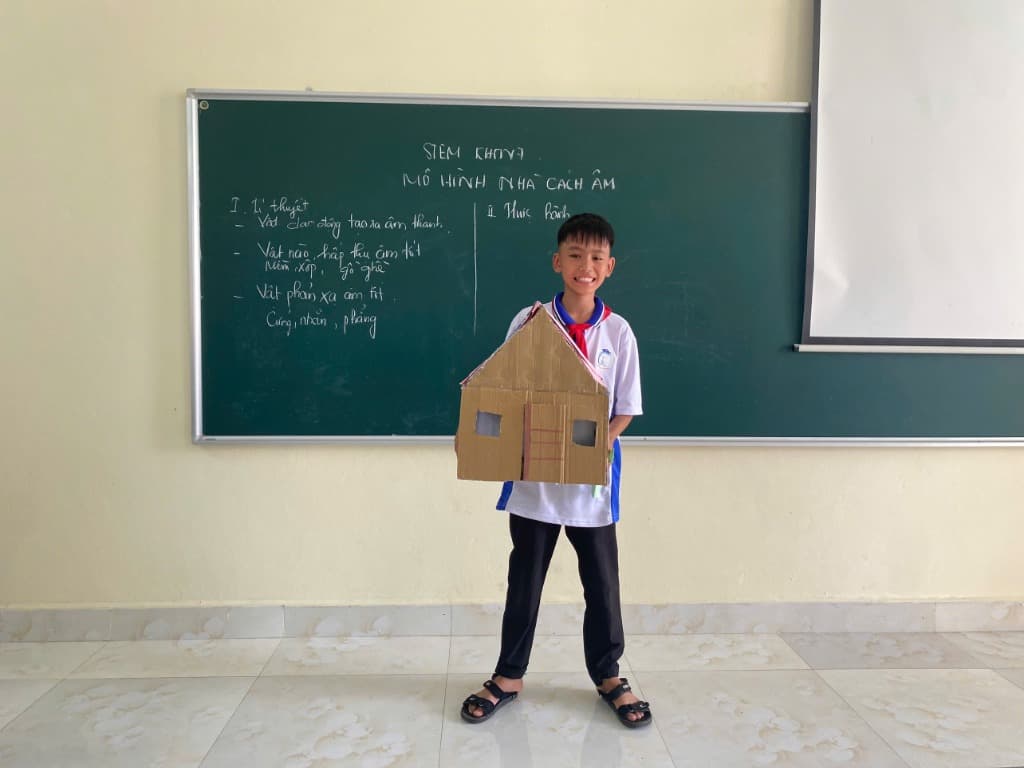 Học sinh nam thuyết trình mô hình nhà cách âm trước bảng